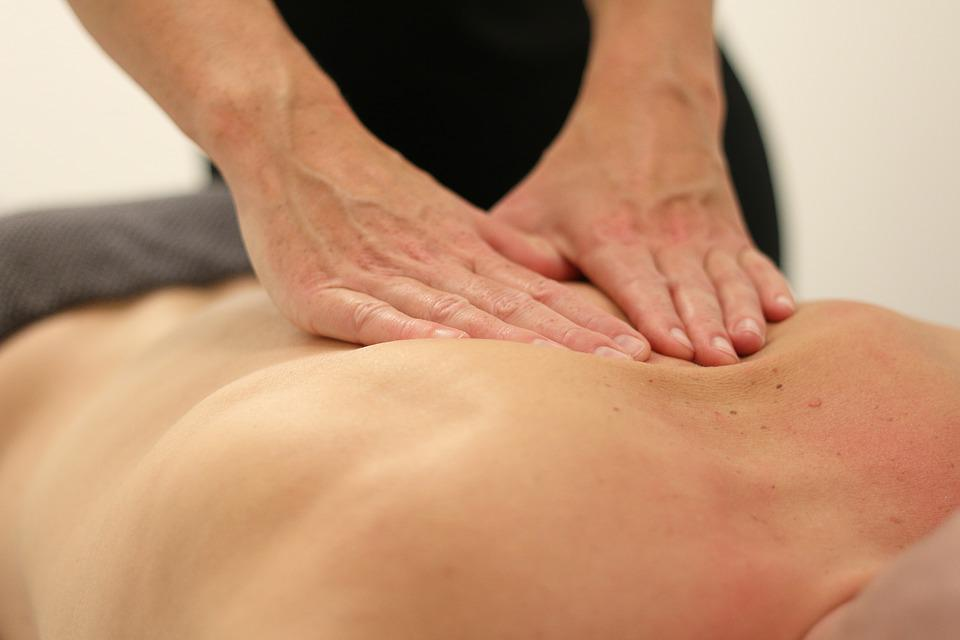 A Faceless Massage Therapist Rubbing a Man’s Back with Both Hands