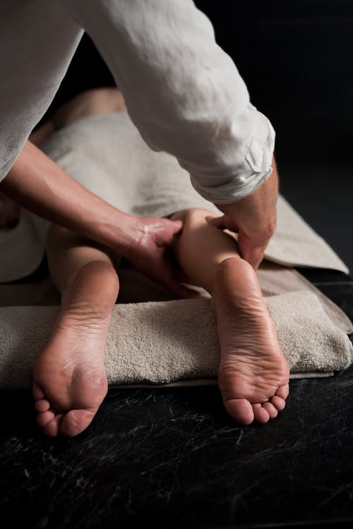 A Massage Therapist Rubbing the Back of a Man’s Calves During an Asian Body Massage