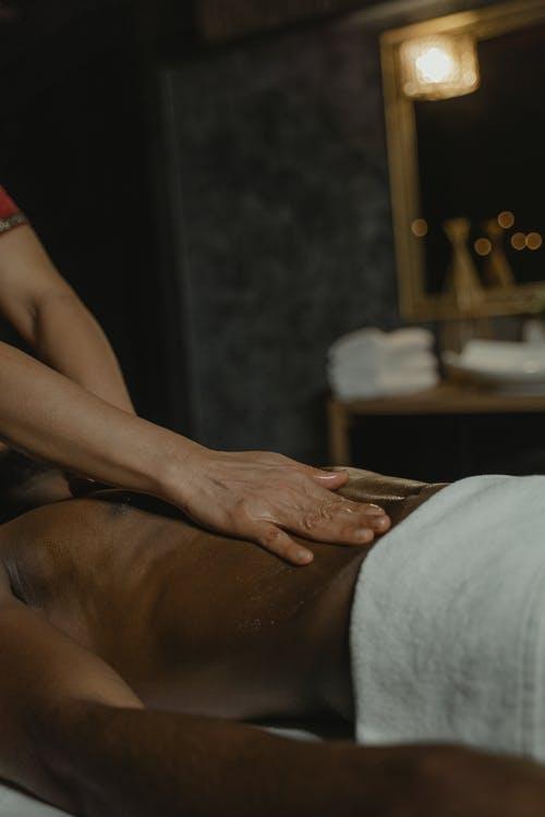  A Faceless Man Lies on his Back as a Massage Therapist Rubs his Abs During a Body Massage