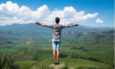 An image of a man standing on an elevated surface while wearing a gray shirt and blue shorts