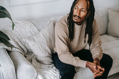 An image of a man sitting on a sofa while looking pensive 