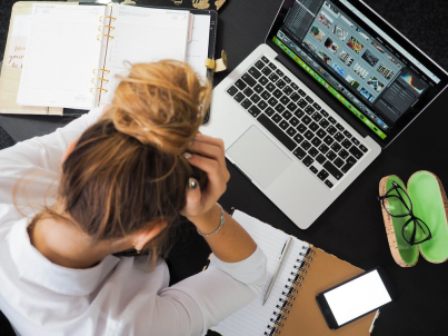 An image of a woman sitting in front of a laptop with her head in her hands