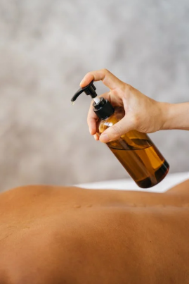 An image of a massage therapist putting massage oil on a person’s bare back 