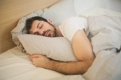 An image of a man in a white shirt sleeping peacefully in his bed  