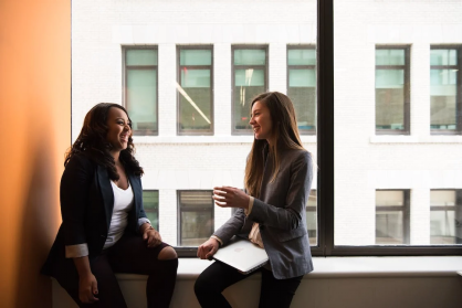 An image of two women chatting while sitting by the window 