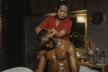 An image of a woman massaging a shirtless man on the head while sitting in a hotel room 