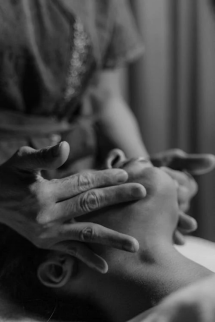 A gray scale image of a female massage therapist massaging a person’s face