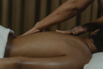 An image of a female massage therapist massaging a person’s bare back with their hands in a dark room 