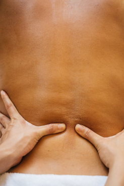 An image of a massage therapist massaging a client’s bare back with their hands