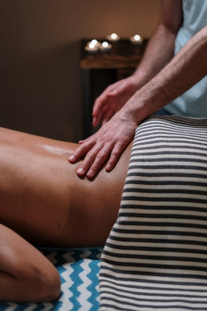 An image of a massage therapist massaging a client’s bare back with their hands 