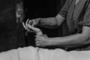 A gray scale image of a massage therapist massaging a client’s hands with their hands 