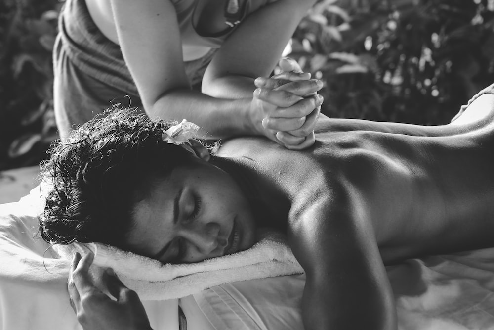 Greyscale photo of a woman receiving a body massage